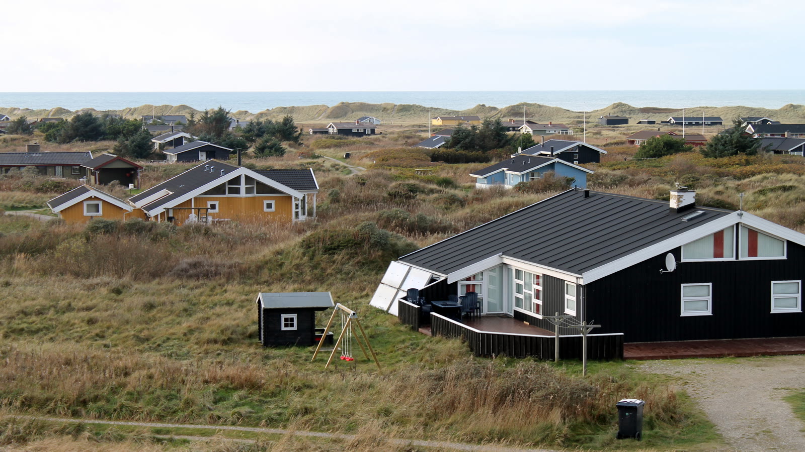 Sort træsommerhus med tagpap i klitlandskab